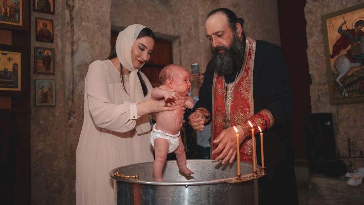 Priest and family performing Orthodox baptism ceremony inside the church.